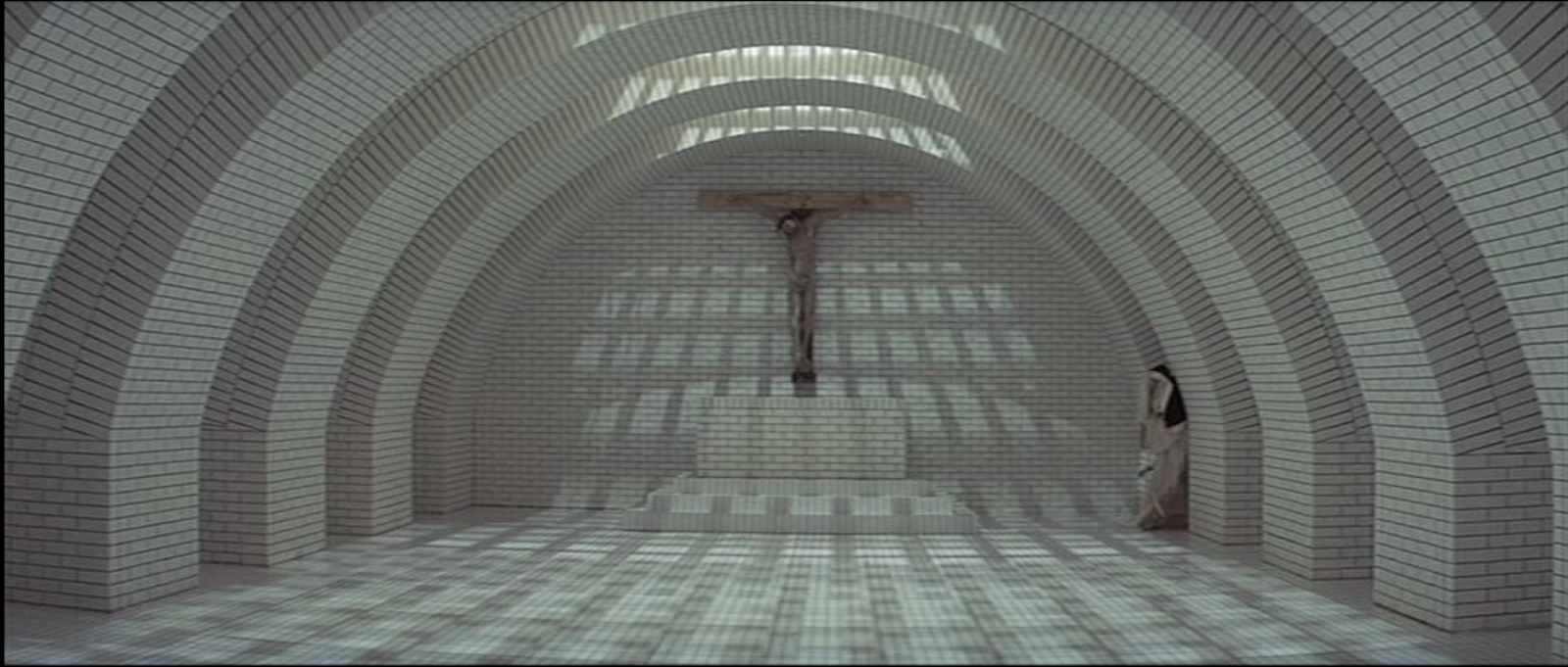 A room with a curved archway of white brick in an intricate pattern. A crucifix with a figure on it is visible from a distance, and a nun's habit is shown in the corner.