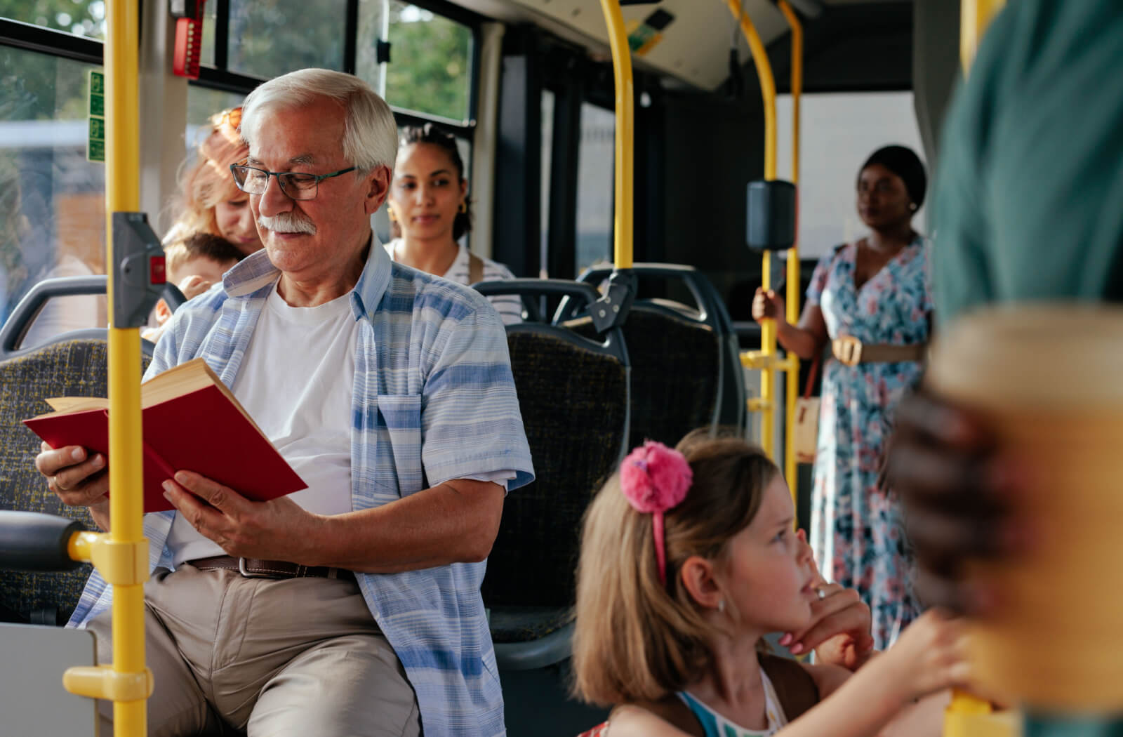 A senior man reading a book while riding a bus to his destination.