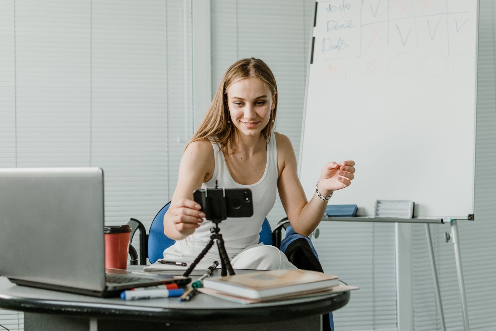 A woman using a phone and tripod to film herself giving a presentation. 