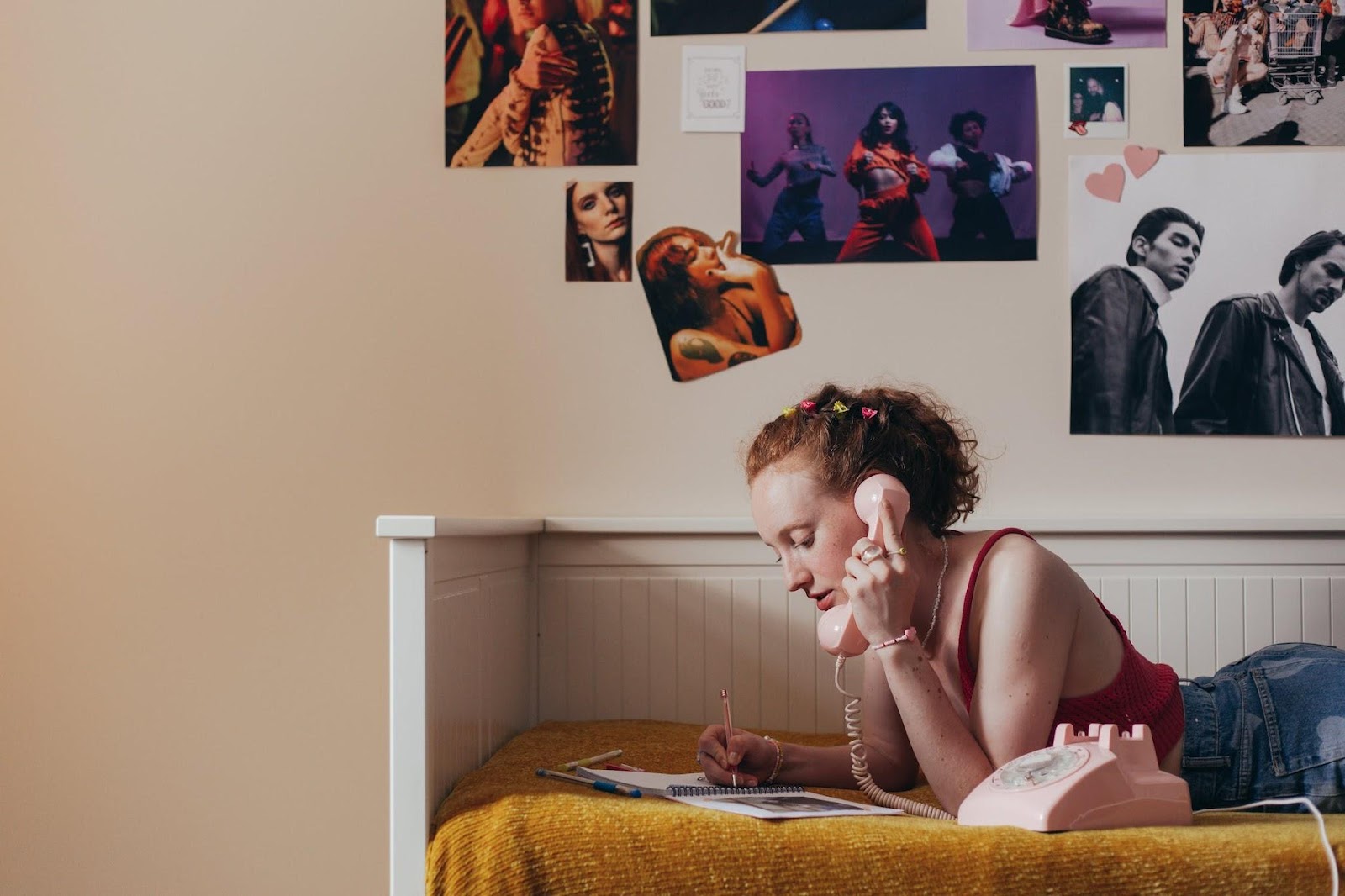 teen in her bedroom on phone on her bed with photos on the wall