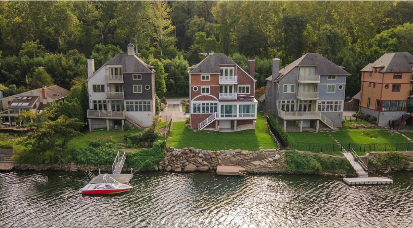 Beautiful multi-story waterfront homes in Gladwyne, Pennsylvania. The homes back up to lush green yards and floating docks on the sparkling waters. The fronts of the homes are surrounded by mature trees. 