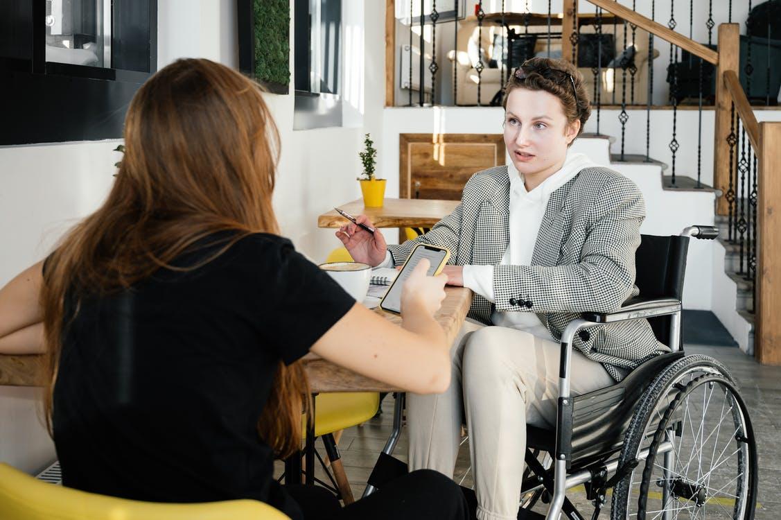 Concentrated female using wheelchair talking to coworker during coffee break in modern cafeteria