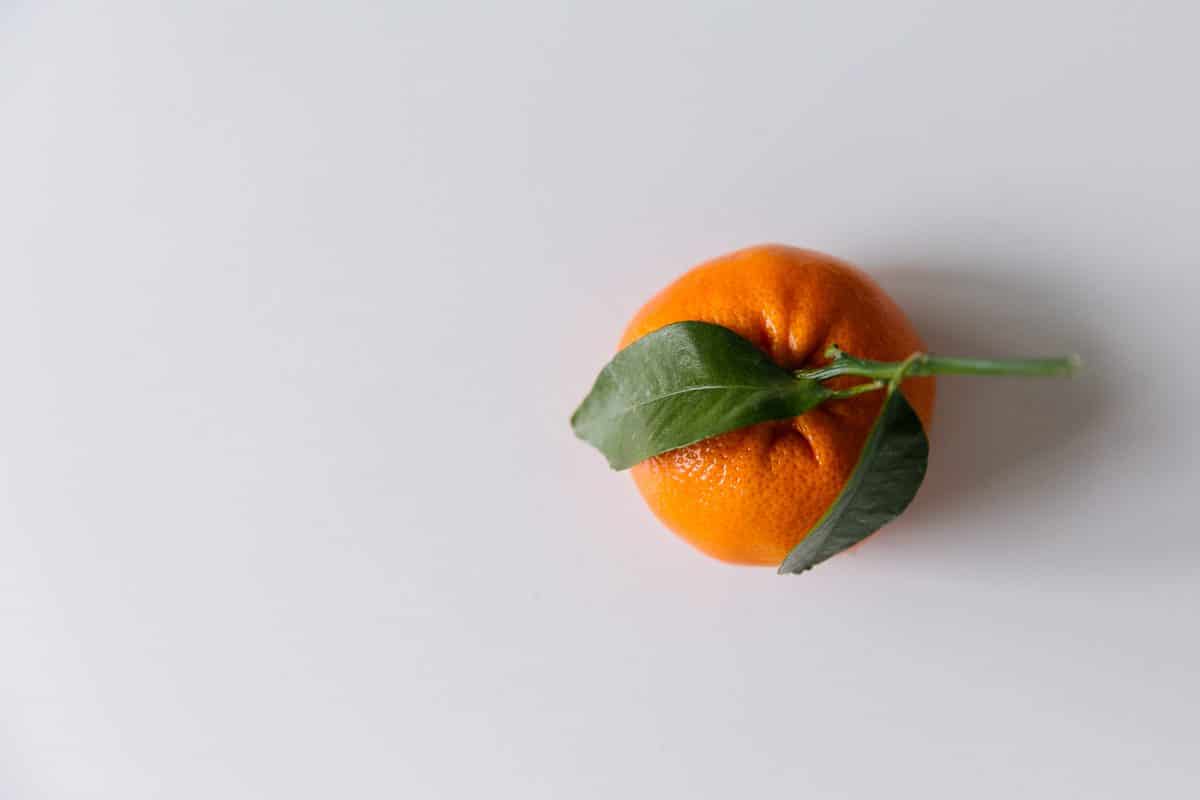 An orange on a white table with two green leaves.