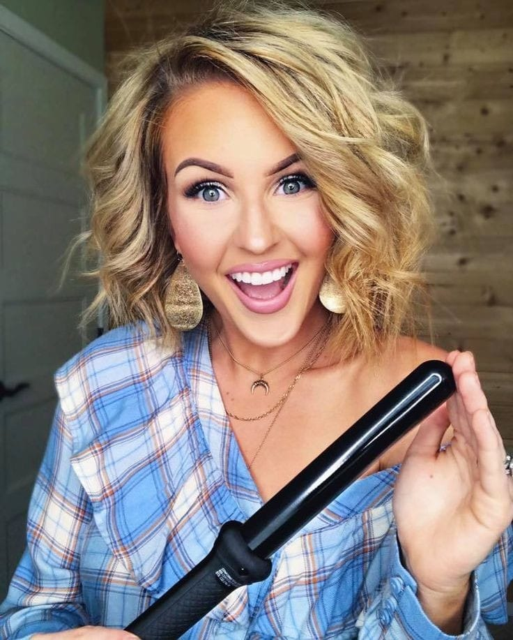 a lady holding a curling wand close to her blonde wavy short hair