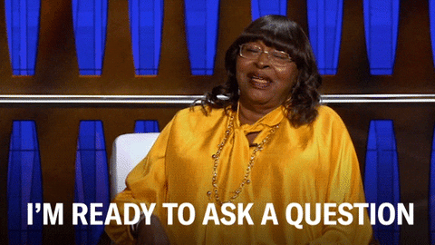 A woman smiling on a game show and raising her hand to point up. The caption says "I'm ready to ask a question".