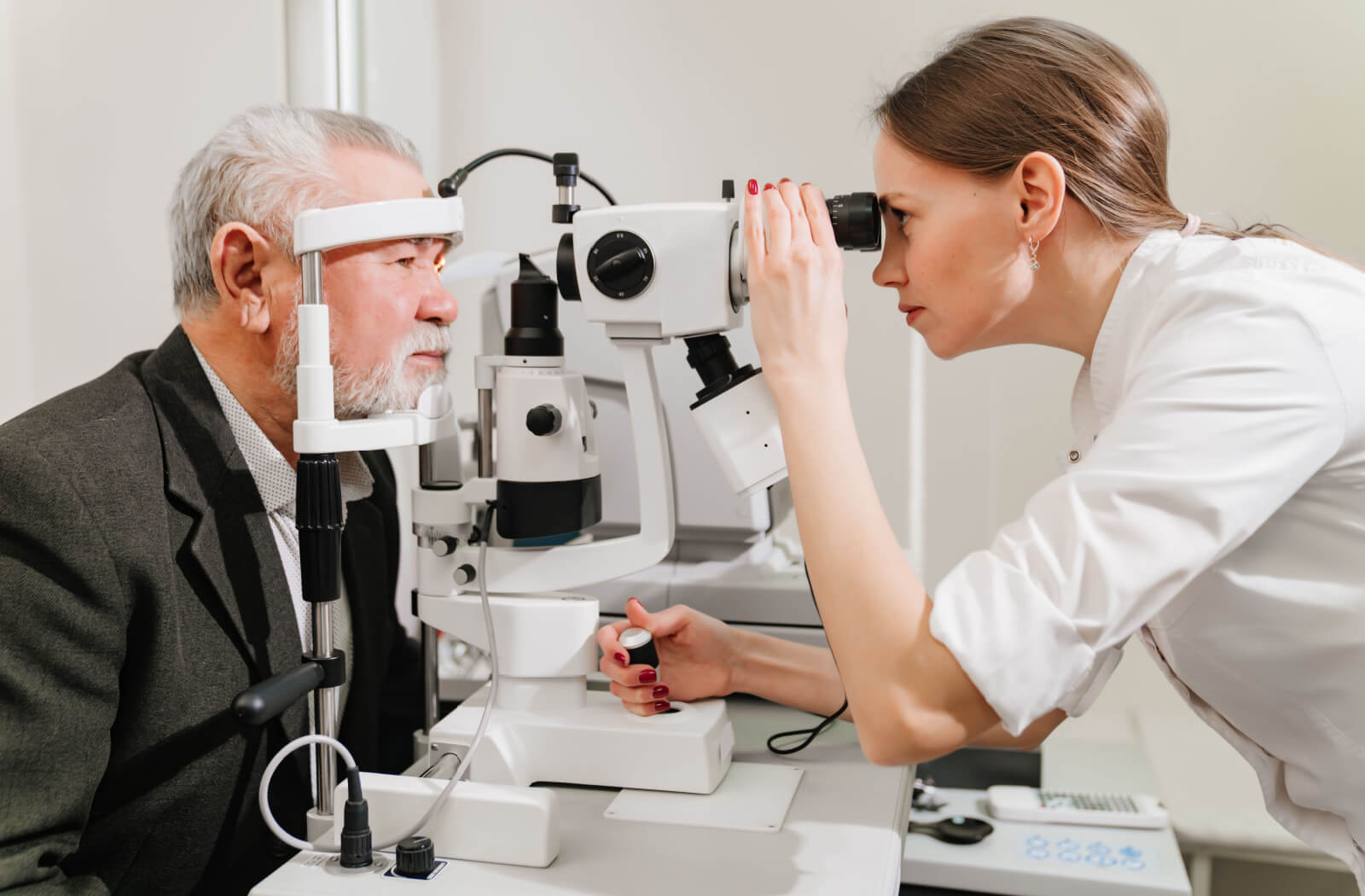 An optometrist using specialized medical equipment to perform an eye exam on a senior male patient.