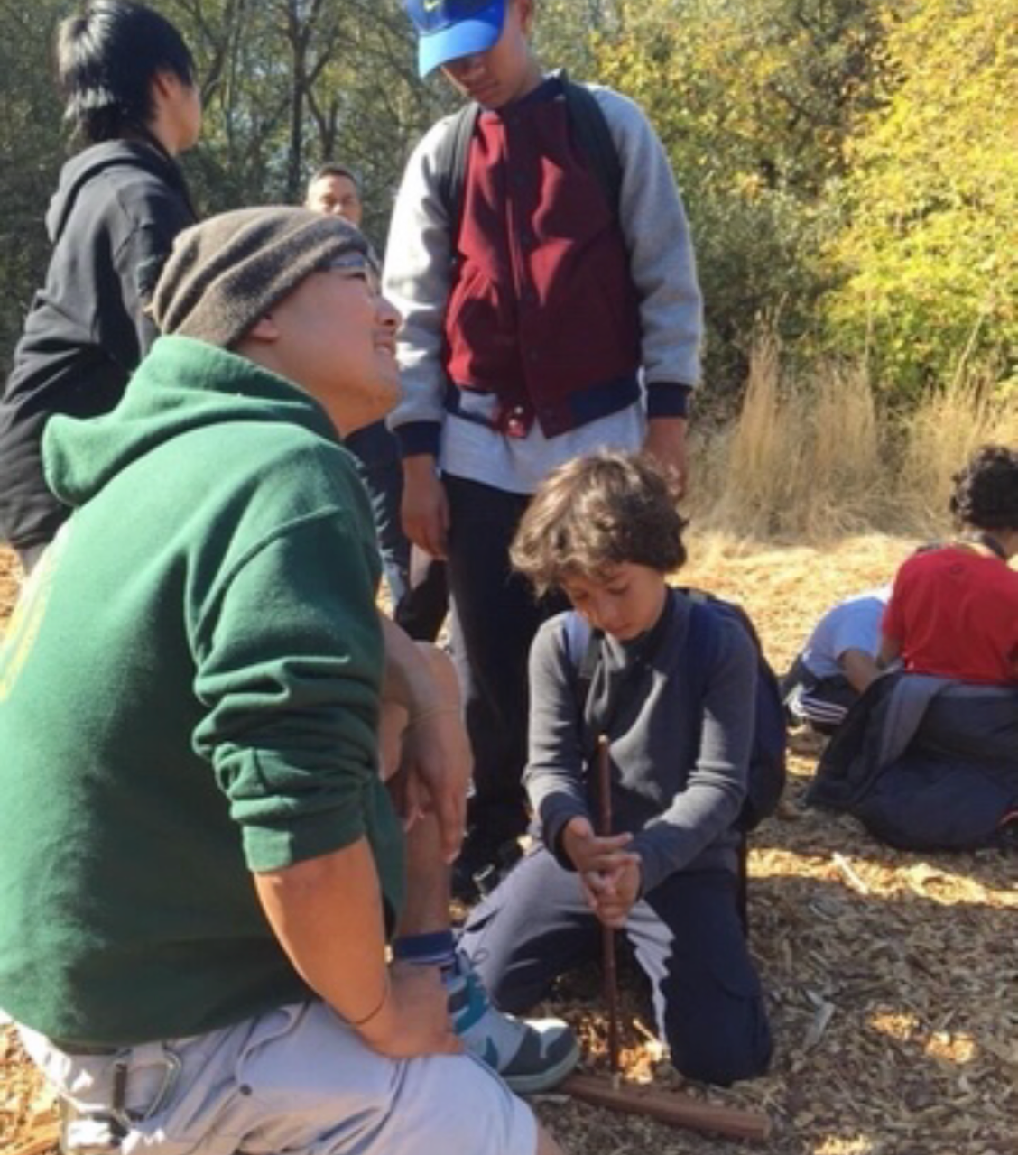 Francis Mendoza teaching a young student how to make fire using an elderberry hand drill and redwood hearth board.