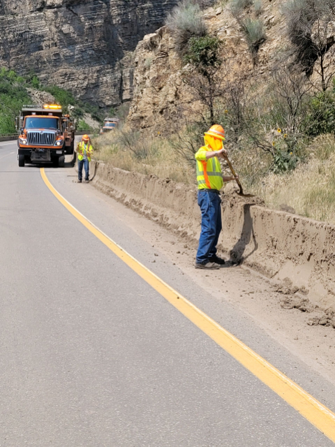 Maintenance workers shovel mud off road barriers