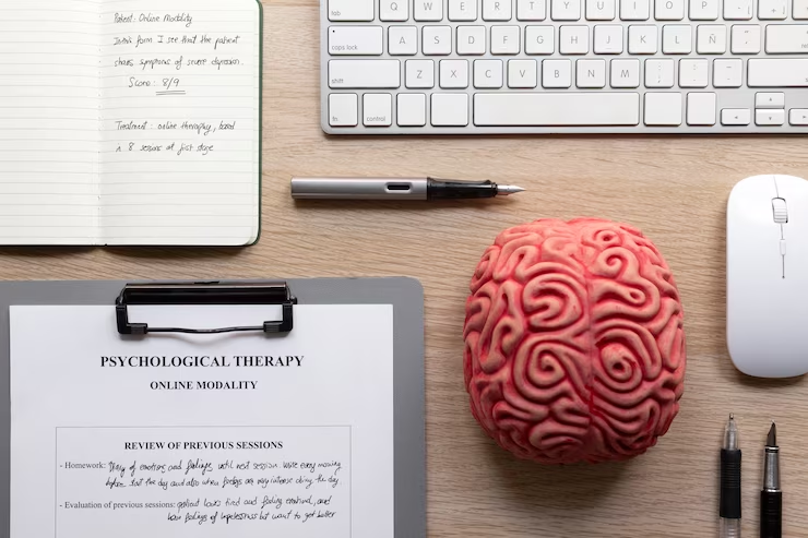 Top view of an online psychologist concept. A laptop with a virtual therapy session interface, notepad, pen, and a brain model on a desk.