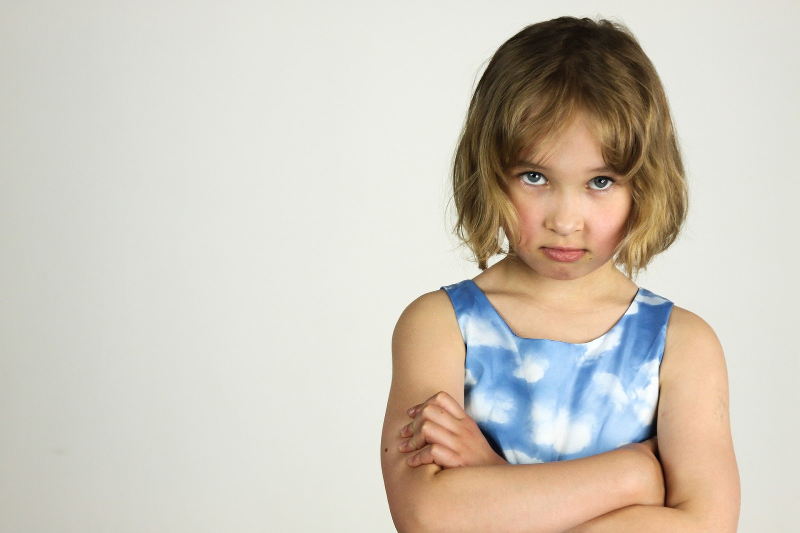 A picture of a young girl, arms folded, looking at the camera with a defiant look on her face.