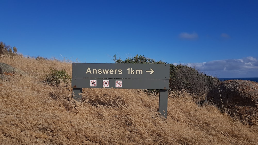 A sign post on a hill in the sun, showing 'Answers 1km'. 