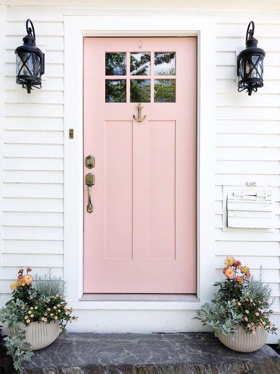 Fachada de casa com porta rosa claro, paredes brancas e vasos de planta no degrau.