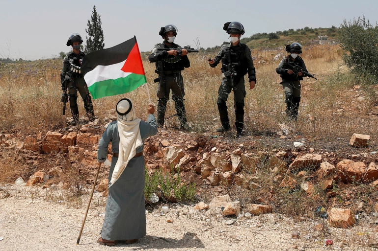 A demonstrator holds a Palestinian flag in front of Israeli forces during a protest against Israel's plan to annex parts of the occupied West Bank, near Tulkarm June 5, 2020 [Mohamad Torokman/Reuters]