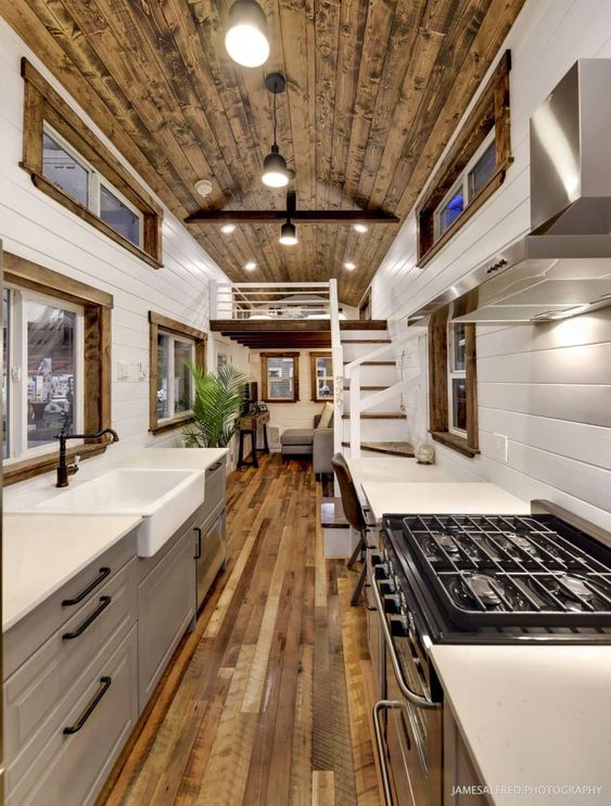 small tiny home kitchen design with wood floors, wood ceiling, grey tiny kitchen cabinets, black hardware, full sized stainless steel stove and range hood, tiny homes like hgtv tiny homes