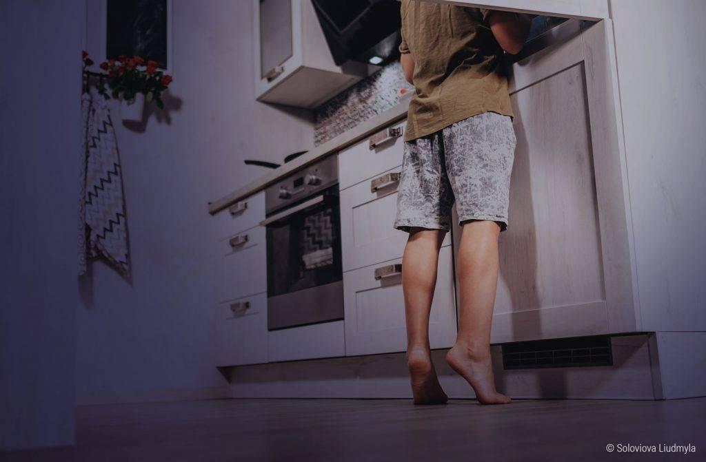 Foto: Una persona está descalza en la cocina por la noche y mira en el refrigerador.
