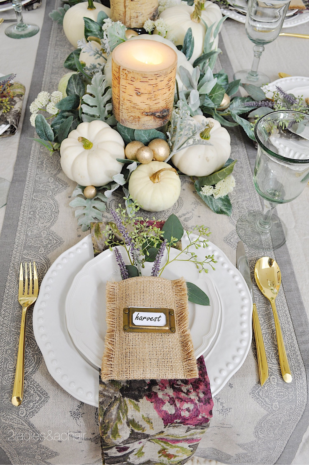 elegant fall table setting with gold silverware, white pumpkins, white candles, green foliage and white dishware