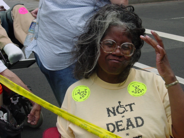 Woman touches her hair in the wind wearing a shirt that says: NOT DEAD.