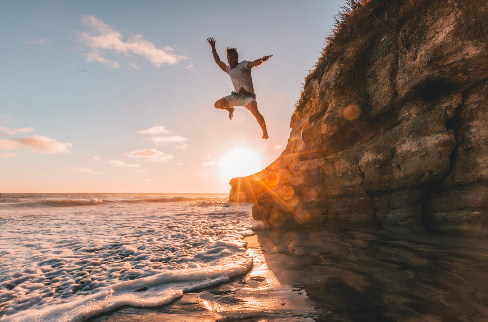 A man jumping off a cliff into the ocean on a hot summer day