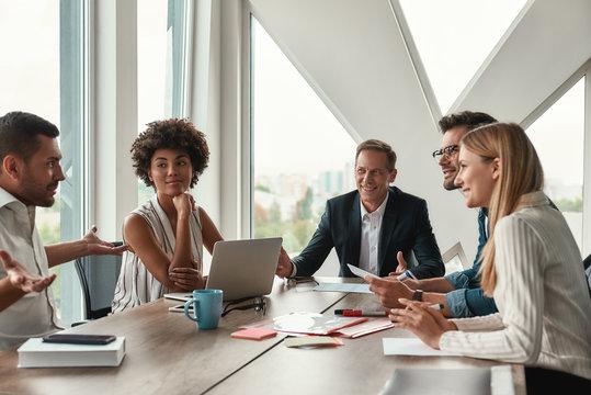 Fresh ideas. Group of young business people discussing something and  smiling while sitting at the office table Stock Photo | Adobe Stock