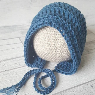 blue baby bonnet on crochet ball sitting on wooden background