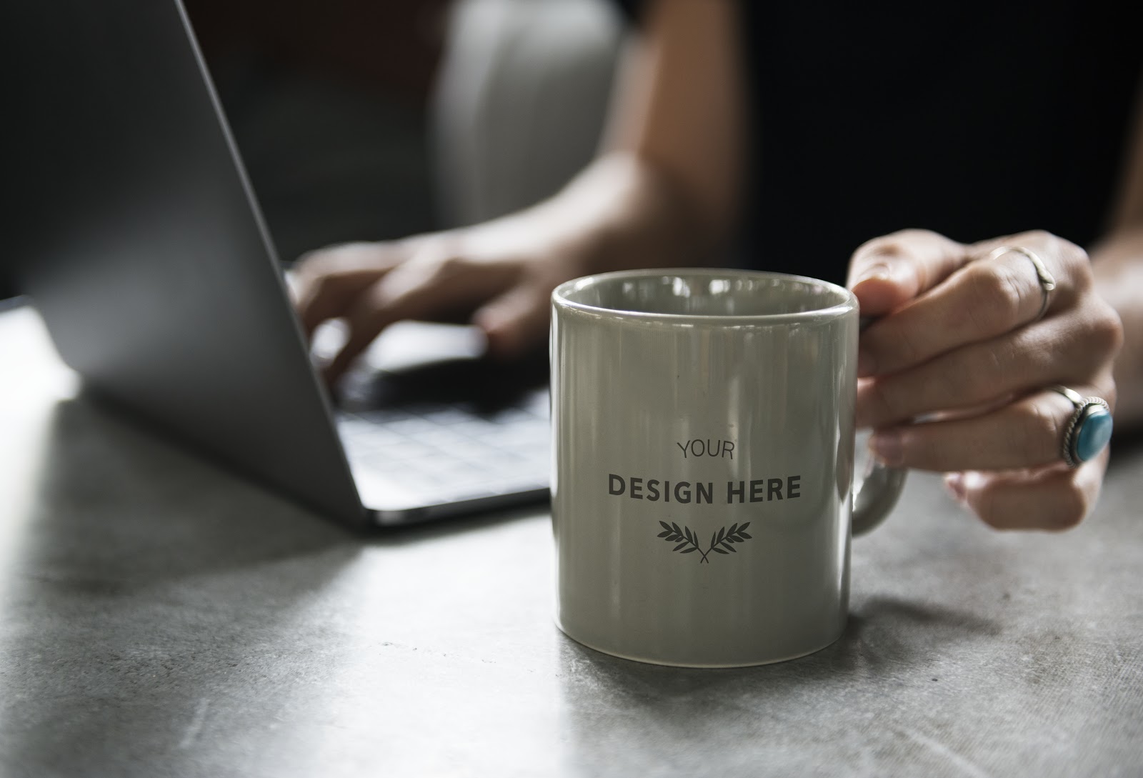 a woman typing on the laptop while holding a grey mug