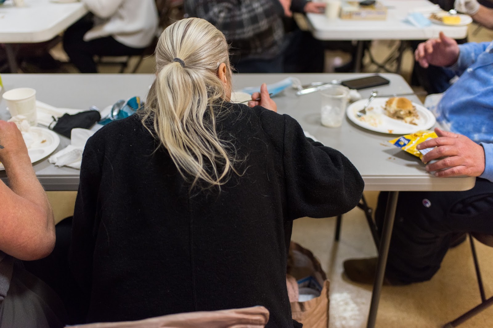 The back of a person with a long ponytail, sitting at a folding table eating.
