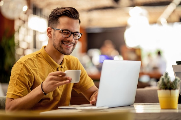 Free photo smiling man surfing the net on laptop while drinking coffee in a bar