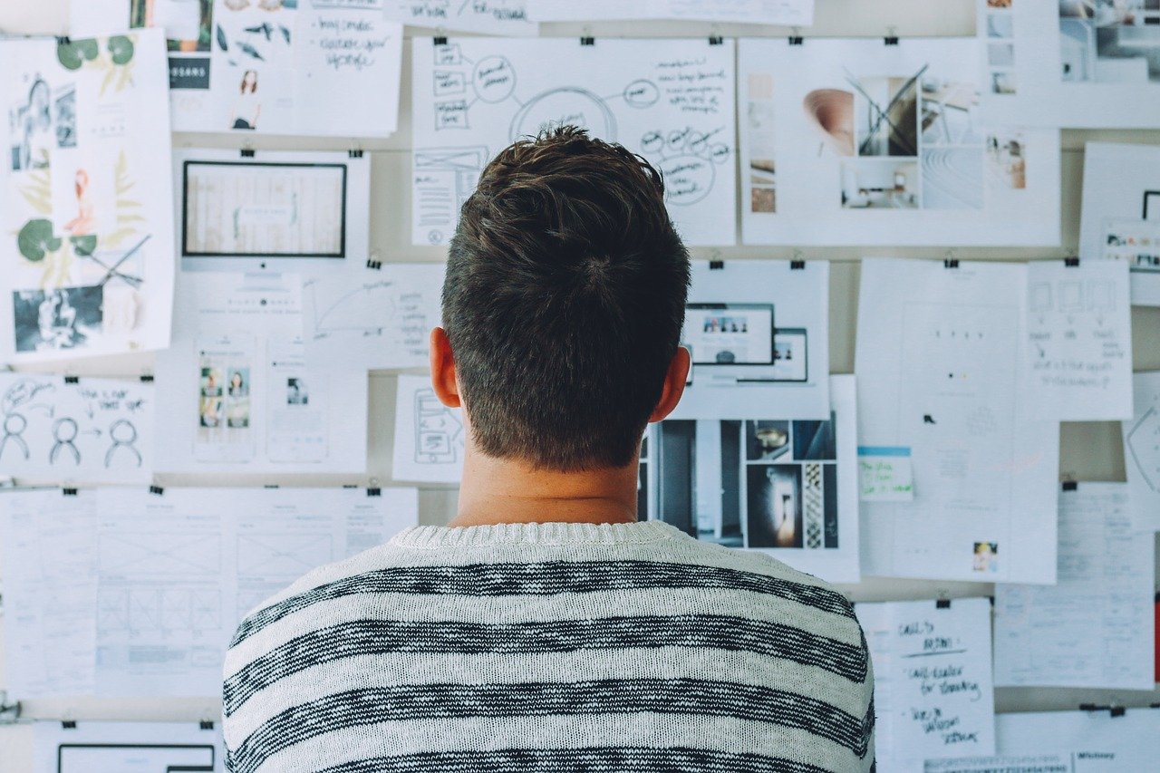 A man standing in front of a wall filled with papers and pictures 