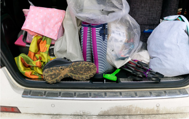 Muddy rain boots, plastic bags, a stroller, and other miscellaneous belongings in the trunk of a white car