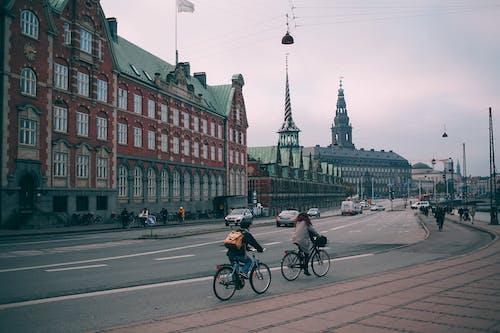 Free Cyclists riding along famous embankment in Copenhagen with historic Christiansborg palace and stock exchange building in Denmark on cloudy day Stock Photo