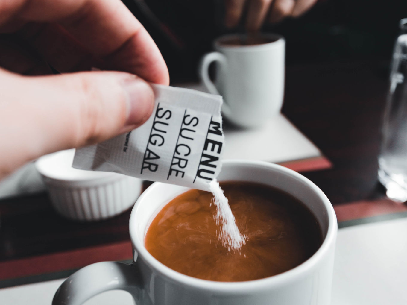 A person emptying a sugar packet on a coffee.