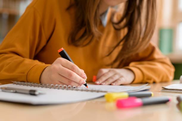 Young unrecognisable female college student in class, taking notes and using highlighter. Focused student in classroom. Authentic Education concept.  writing assignment stock pictures, royalty-free photos & images