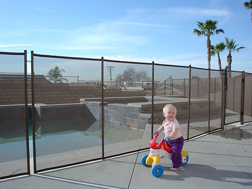 Toddler on a trike in front of a black removable swimming pool fence
