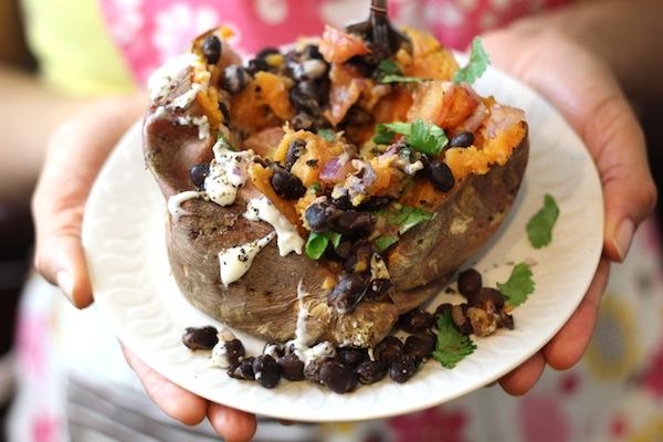 Side View of hands holding plate of Stuffed Ranchero Sweet Potato