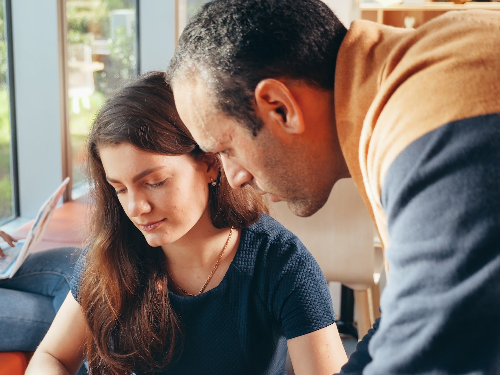 A man looks over a teenage girl's shoulder. They seem to be considering something, like scheduling options for high school STEM courses.