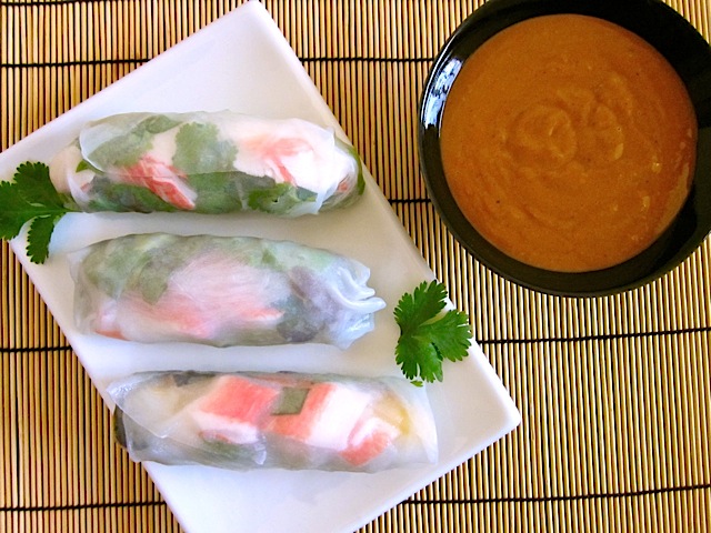 Three spring rolls on white plate with small bowl of peanut sauce on the side 