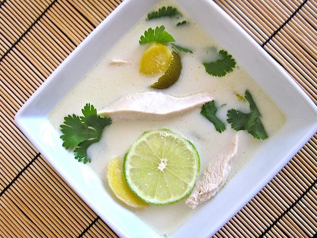Overhead view of a square bowl of chicken coconut soup with a slice of fresh lime