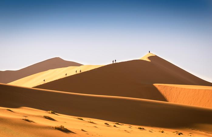 Drumeții călare pe dunele ce par întinse până la capătul pământului