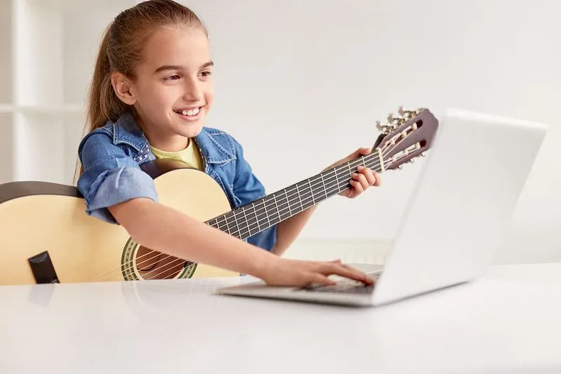 menina branca com cabelo preso em um rabo de cavalo e acompanhada do seu violão, busca na internet possibilidades para música