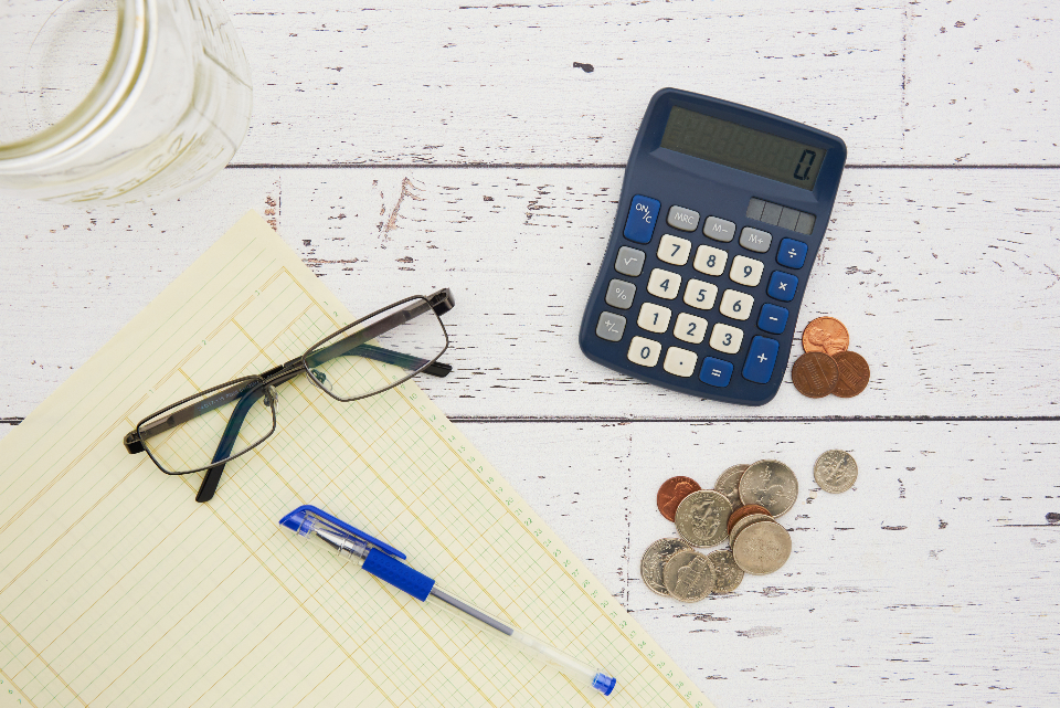 como economizar no seguro: papel, moedas, calculadora, óculos e caneta em cima da mesa. 