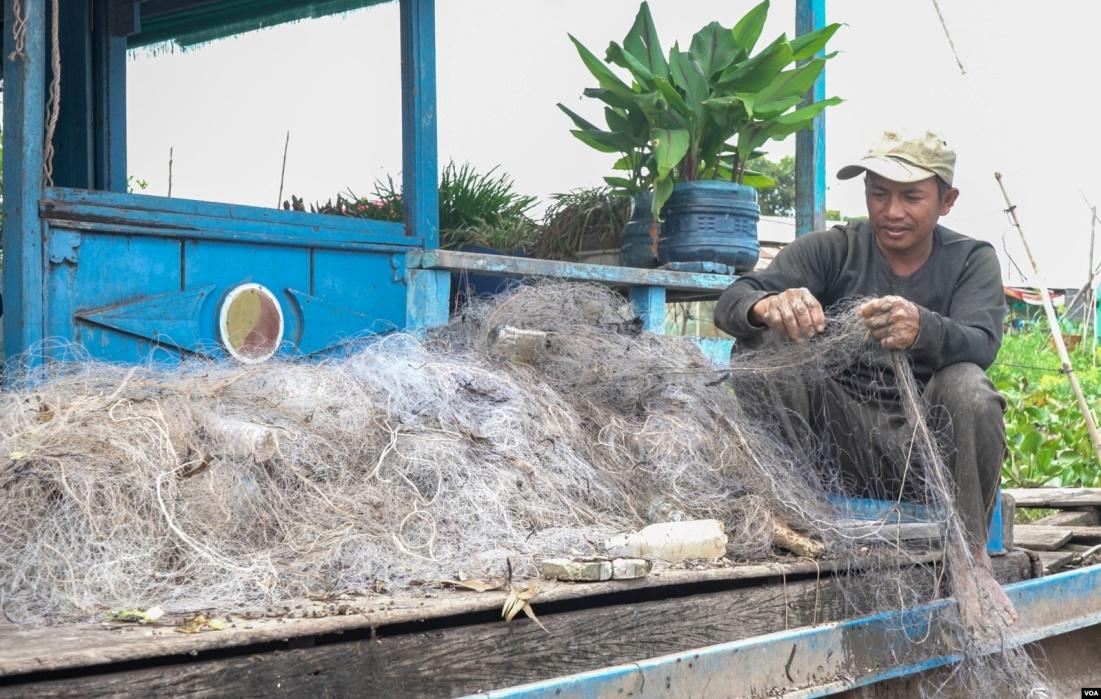 Sout To cleans up the gill nets in front of his floating house in Peam Bang village of Kampong Thom province, on May 04, 2022. (Khan Sokummono/VOA Khmer)