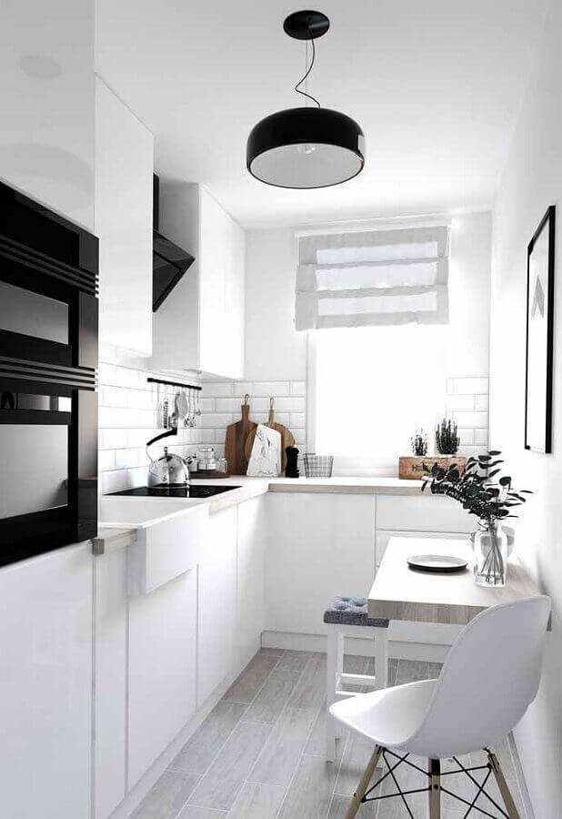 Cozinha com mobília branca, piso de madeira clara, eletrodomésticos pretos, luminária pendente preta e mesinha de madeira clara de canto com cadeira branca.