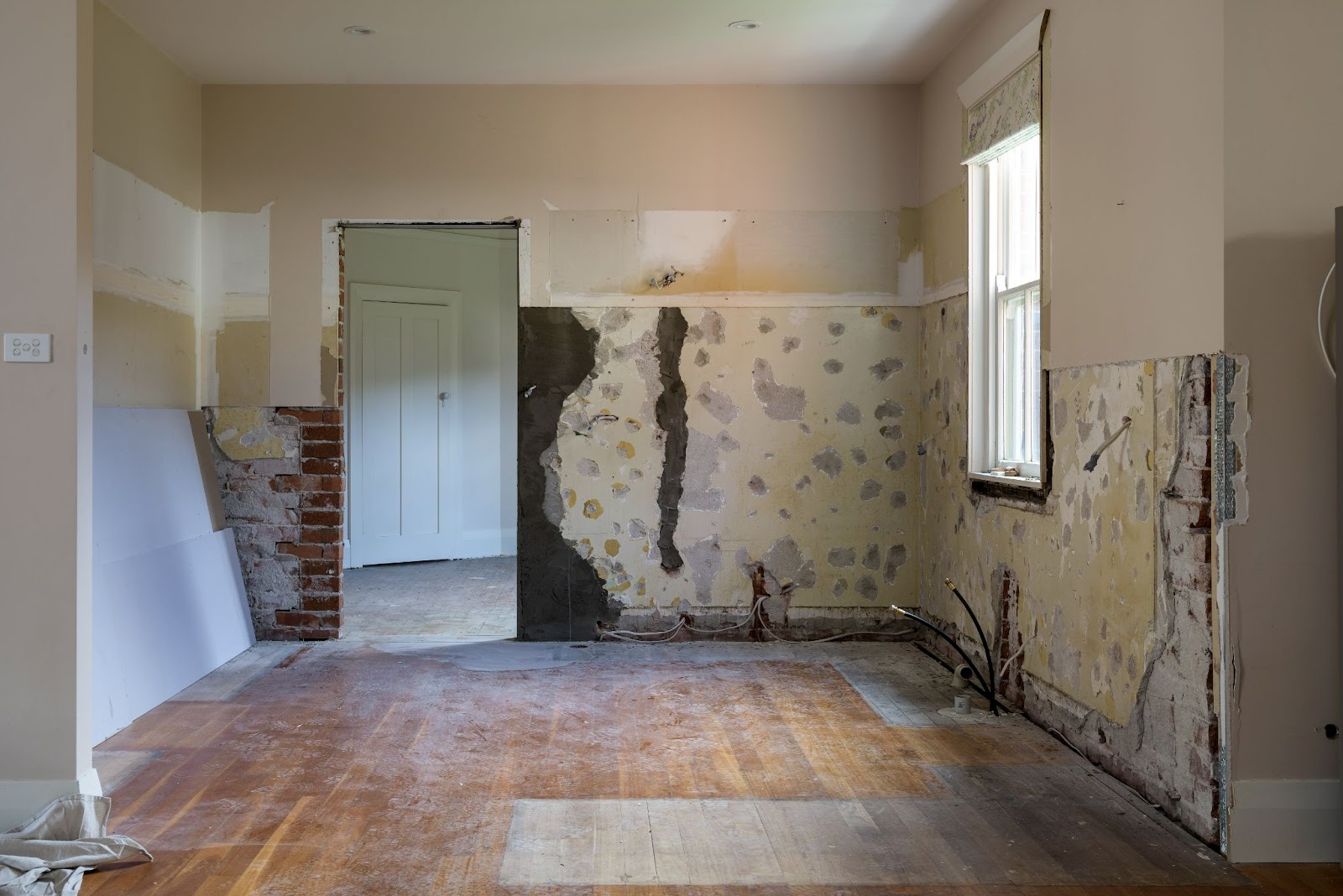 Partially renovated room with exposed brick and plaster, bare walls, and an unfinished floor, highlighting the early stages of a home renovation.