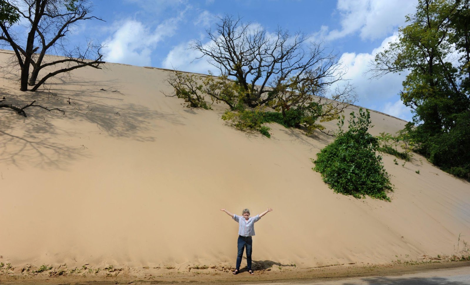 A woman standing with arms wide open in front of Mount Baldy Sand Dune at Indiana Dunes National Park