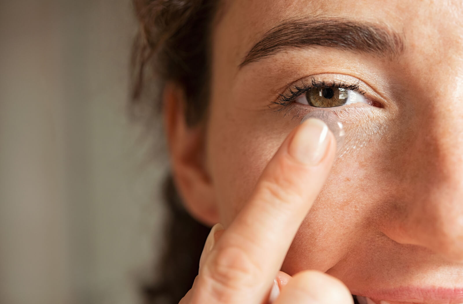 A close-up of a young woman who is about to put on a contact lens on her right eye.