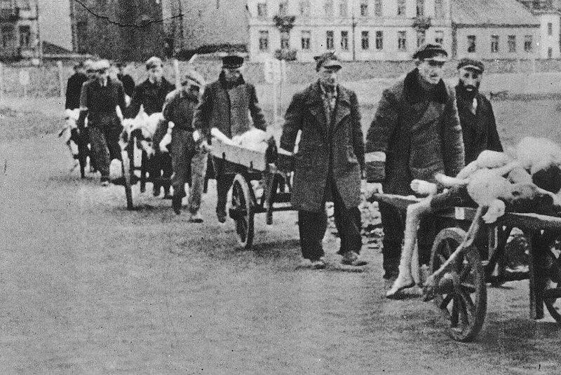 Photograph of men pushing wheelbarrows full of corpses in the Warsaw ghetto.
