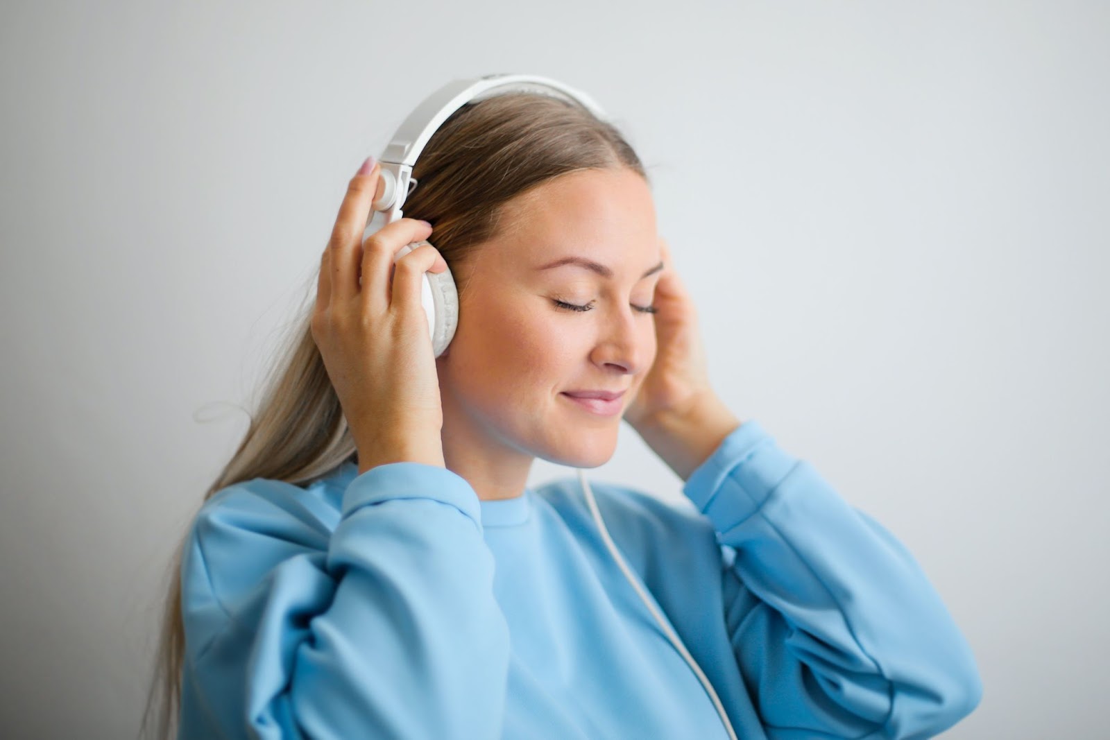 A lady wearing a light -blue sweatshirt listening to music on her whiter headphones - A list of the best Music APIs