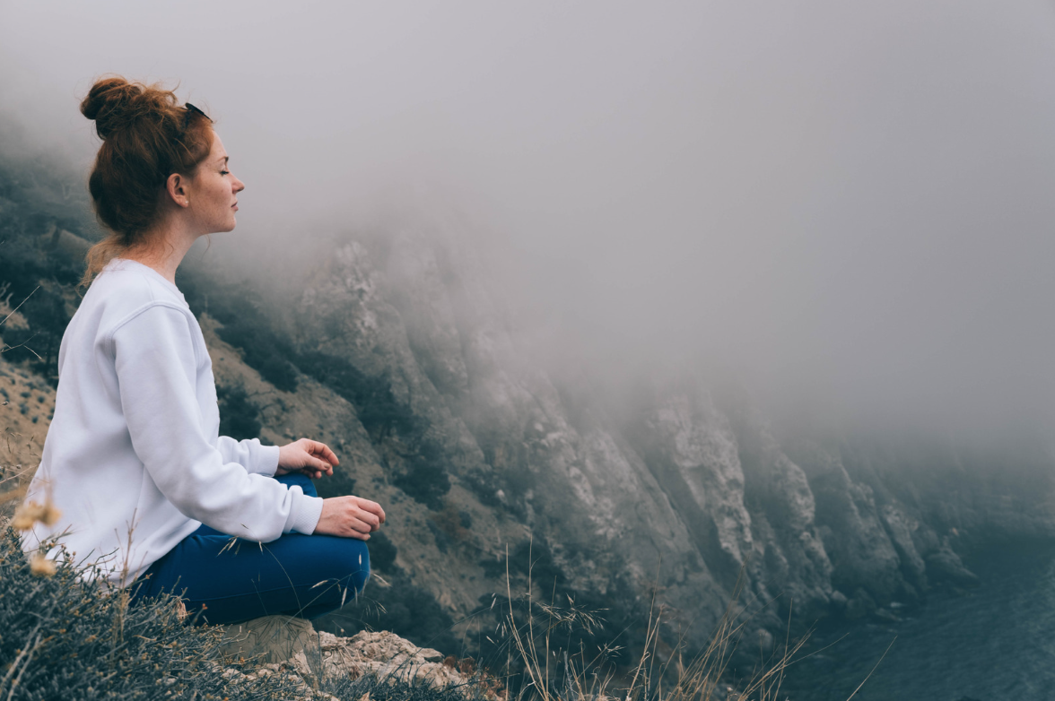 Woman meditating on foggy mountain, peaceful and calm