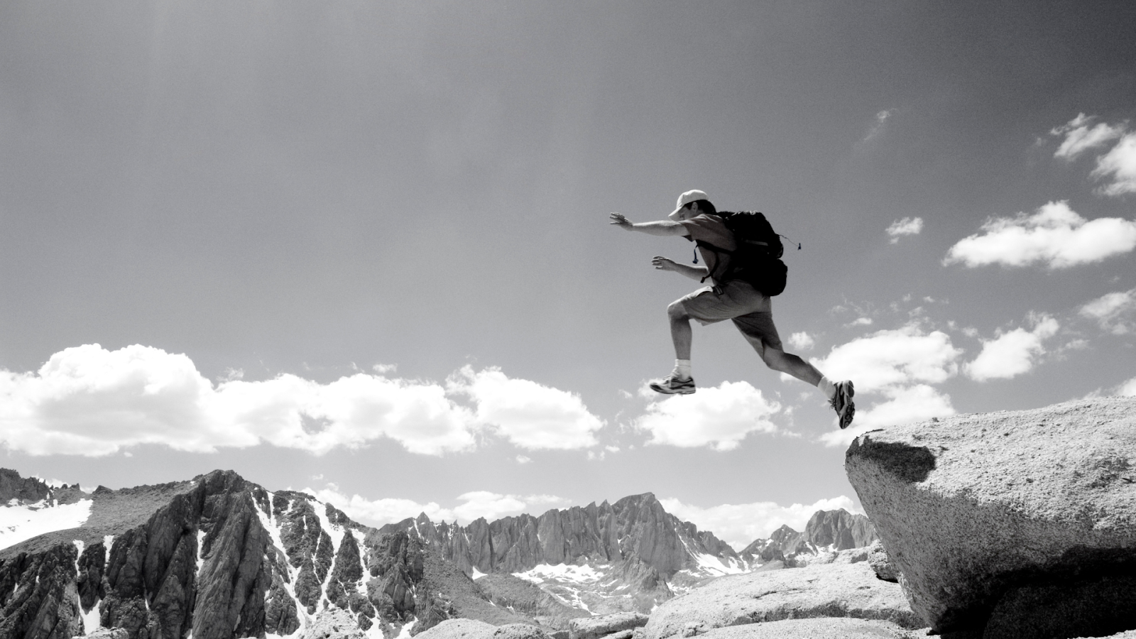 man with backpack jumping off a cliff