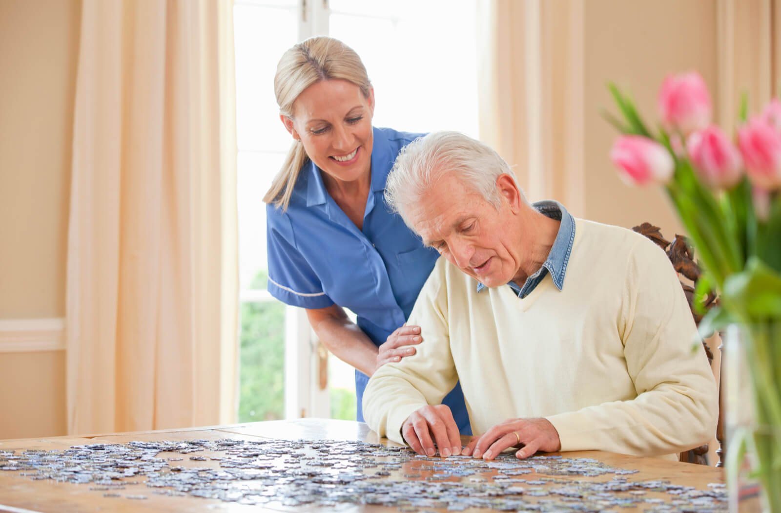 a nurse and a senior man are in a respite home, working on a puzzle together